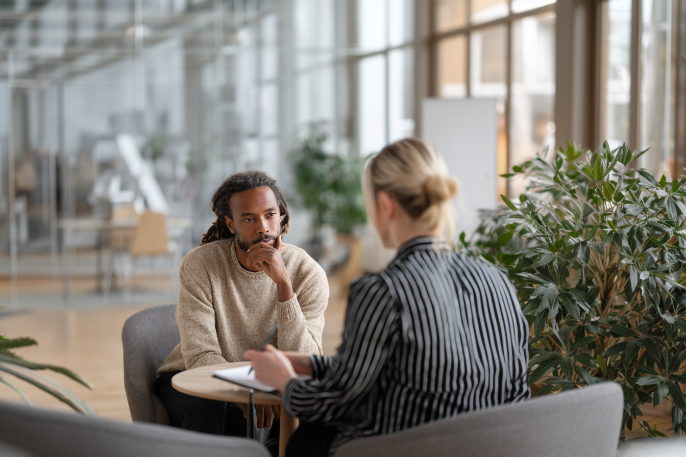 Entretien professionnel dans un cadre chaleureux. Deux personnes discutant autour d’une table dans un espace convivial, tasse de café à la main.